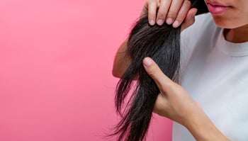 asian-woman-with-dry-lips-holding-damaged-hair-on-pink-background-dry-and-brittle-black-long-hair